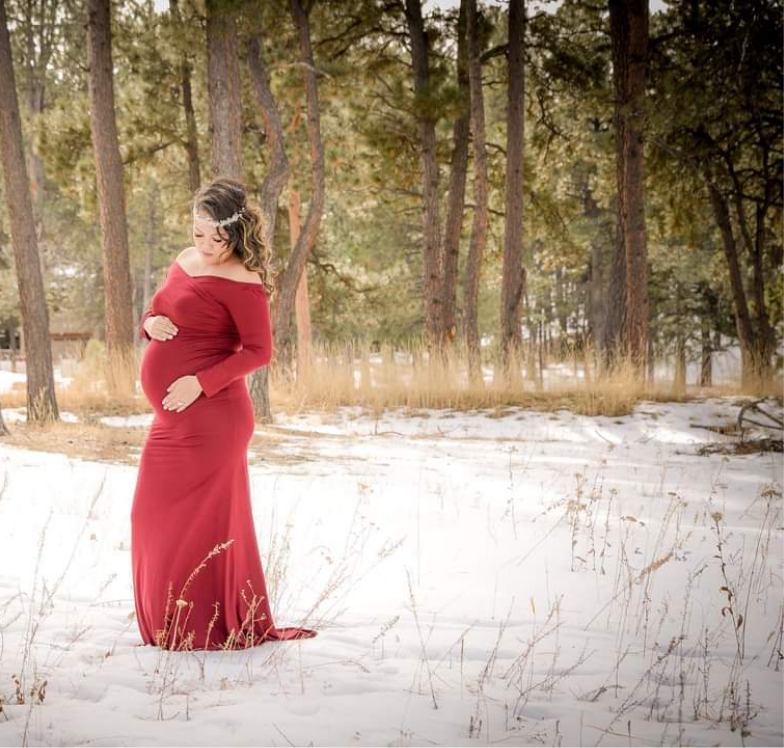 a pregnant woman in a long red maternity dress standing in the snow